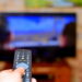 The man with the remote control in hand watching the sports channel and presses the button on the remote control. Remote control in hand closeup.