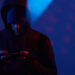 Image of computer hacker in black clothing standing and using his mobile phone in dark room