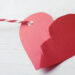 Broken red paper heart and rope on white wooden table, closeup. Cheating concept