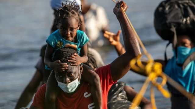 Niña haitiana en los hombros de quien se presume es su padre, ambos migran hacia los Estados Unindos