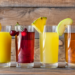 Surtido de jugos de frutas en vasos de cristal. De izquierda a derecha: kiwi, naranja, cereza, piña, manzana y fresa.