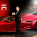 Elon Musk frente a una audiencia, al lado de un Tesla rojo - limpiacristales