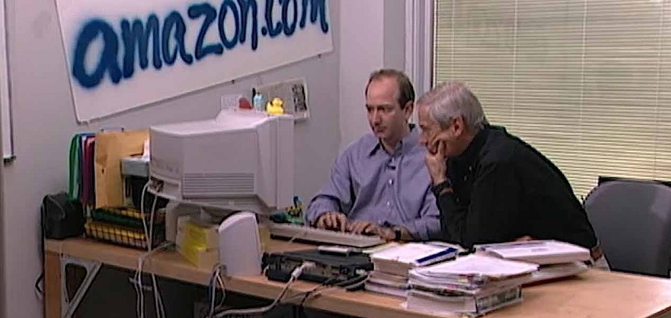 Jeff Bezos acompañado en su primera oficina; cartel de 'amazon.com' pintado en spray colgado en pared