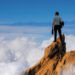 hombre de negocios de pie en la cima del acantilado de la montaña sobre las nubes