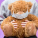 Niño sostiene oso de peluche con mascarilla, coronavirus infantil