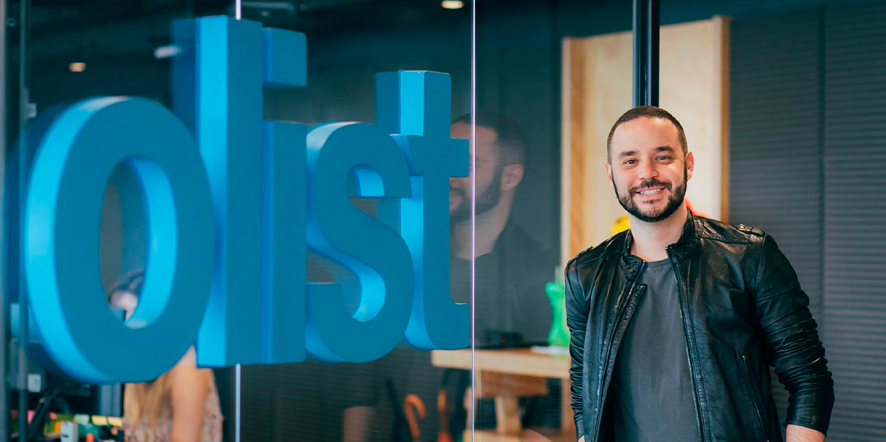 Tiago Dalvi, CEO, recostado de cristal divisor con logo de Olist