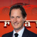 John Elkann sonríe; fondo de vehículo Ferrari y logo