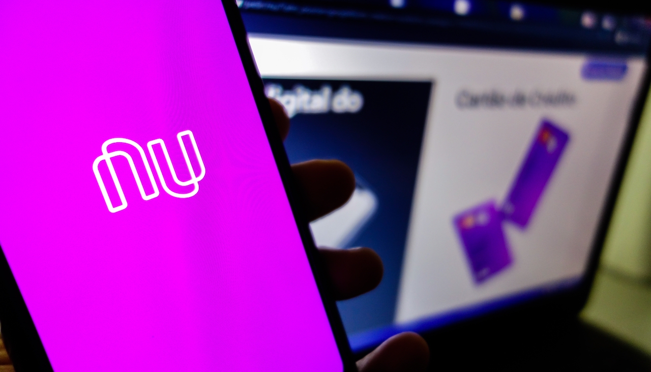 Nubank brazilian fintech logo visible on smartphone screen, and website homepage on background. High quality photo