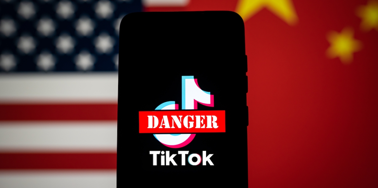 TikTok app logo crossed out with red Danger sign displayed on phone screen with the US and China flags background. Tik Tok ban in the USA concept. Swansea, UK - February 23, 2023.